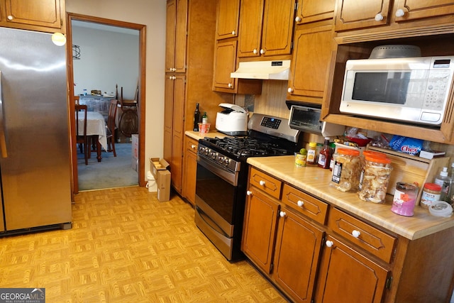 kitchen featuring under cabinet range hood, appliances with stainless steel finishes, light countertops, and brown cabinetry