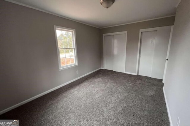 unfurnished bedroom featuring dark colored carpet, ornamental molding, and two closets