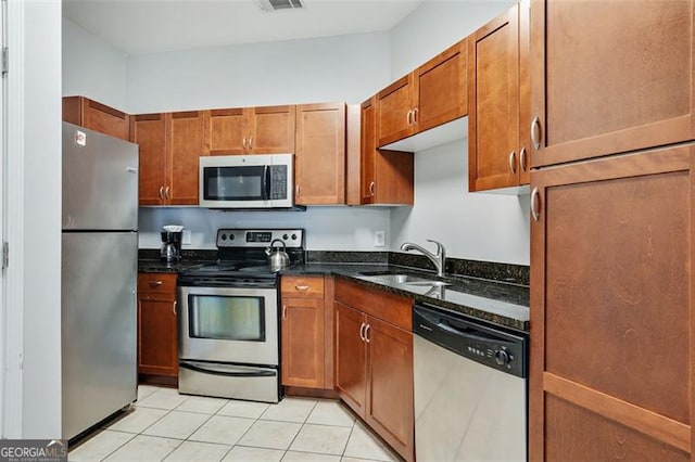 kitchen featuring dark stone countertops, sink, light tile patterned floors, and appliances with stainless steel finishes