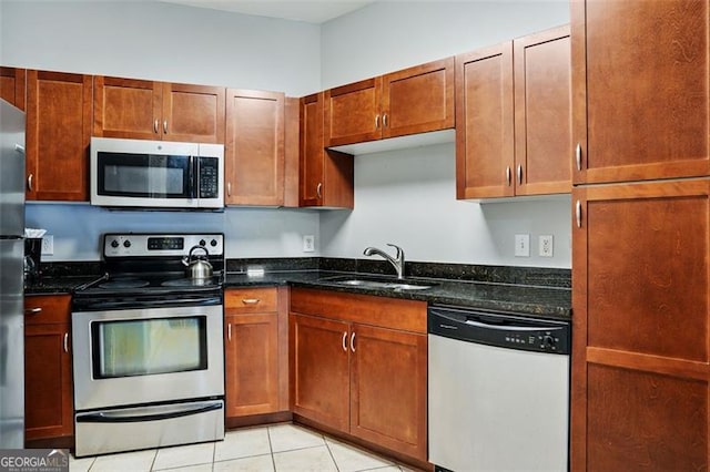 kitchen featuring light tile patterned floors, stainless steel appliances, sink, and dark stone counters