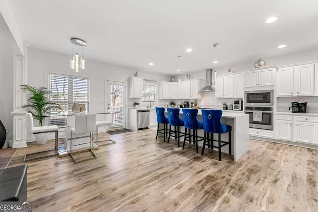 kitchen featuring white cabinets, appliances with stainless steel finishes, hanging light fixtures, and wall chimney range hood