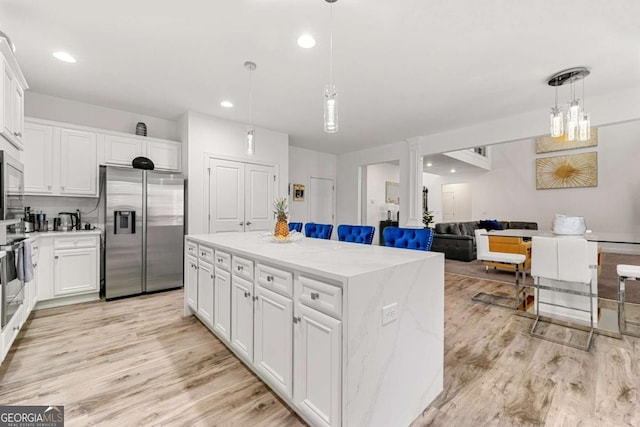 kitchen featuring stainless steel refrigerator with ice dispenser, white cabinetry, decorative light fixtures, and a kitchen island