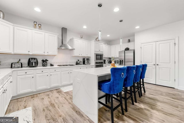 kitchen with wall chimney range hood, stainless steel appliances, a center island, and white cabinets