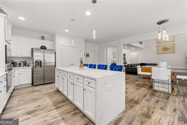 kitchen featuring stainless steel appliances, white cabinetry, a kitchen island, and light stone countertops