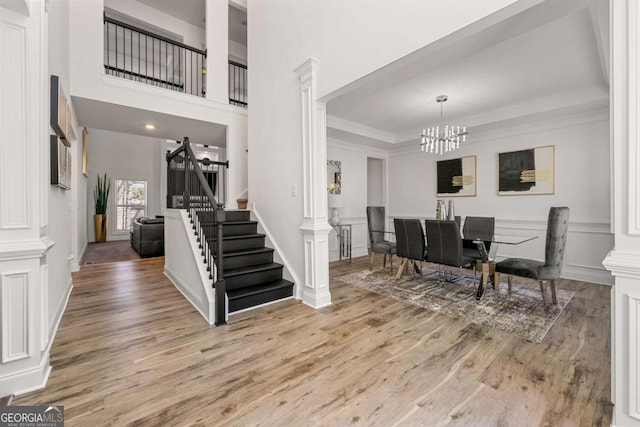 entryway featuring decorative columns, ornamental molding, a chandelier, and light wood-type flooring