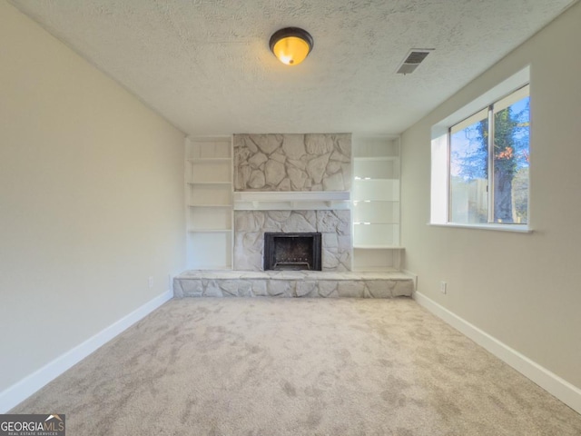 unfurnished living room with a stone fireplace, built in shelves, a textured ceiling, and carpet flooring