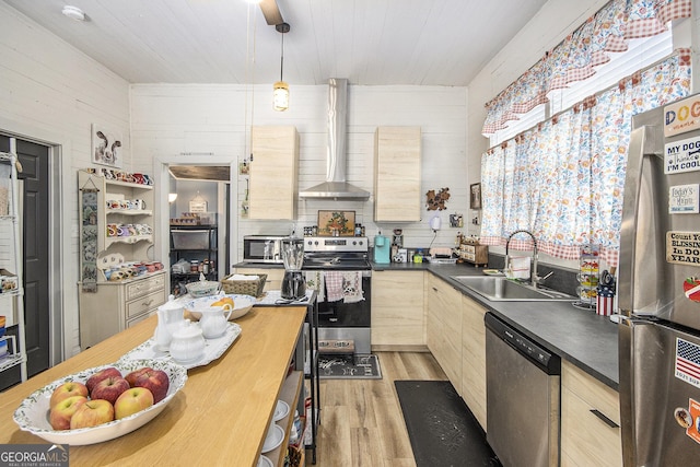 kitchen featuring sink, appliances with stainless steel finishes, wood walls, wall chimney exhaust hood, and light wood-type flooring