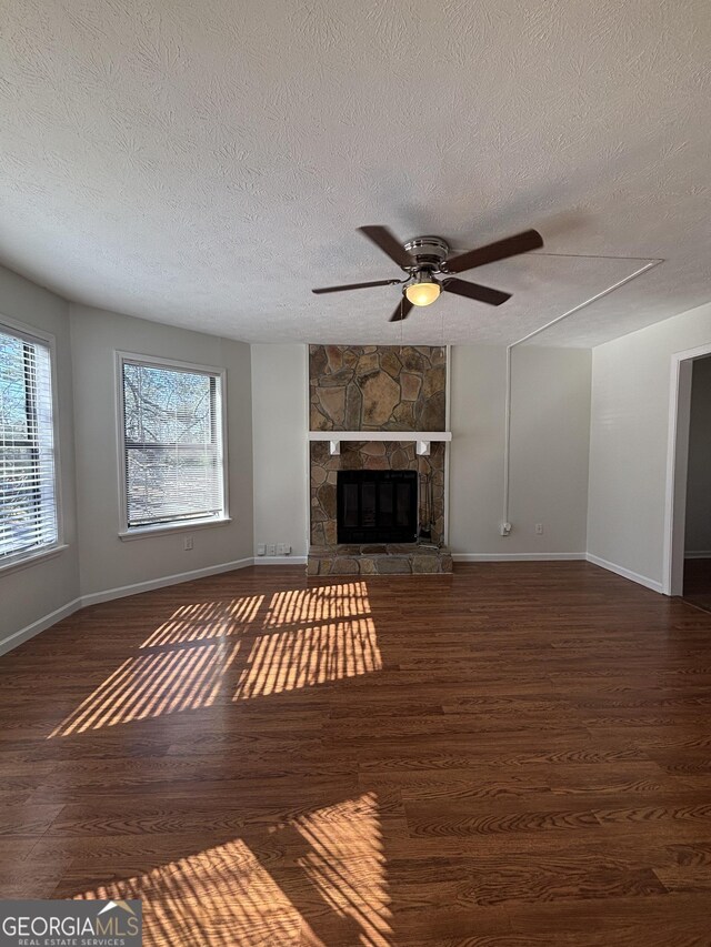 unfurnished living room with a stone fireplace, dark hardwood / wood-style floors, a textured ceiling, and ceiling fan