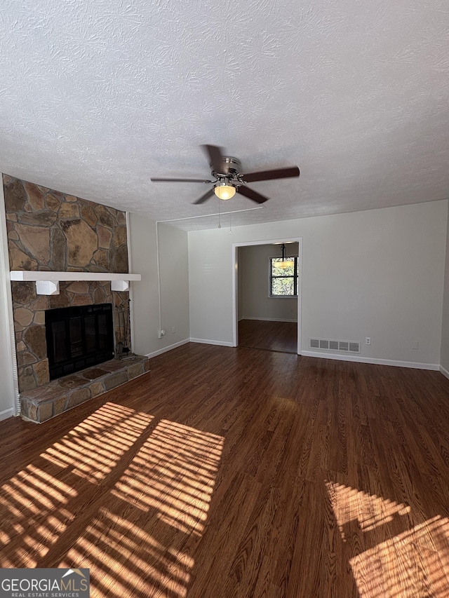 unfurnished living room with ceiling fan, a stone fireplace, a textured ceiling, and dark hardwood / wood-style flooring