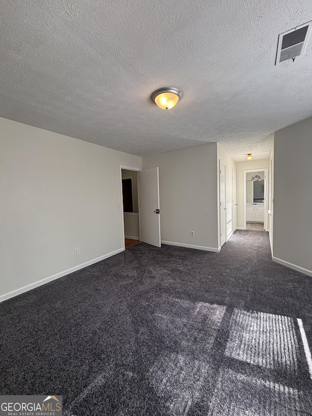 empty room with a textured ceiling and dark colored carpet