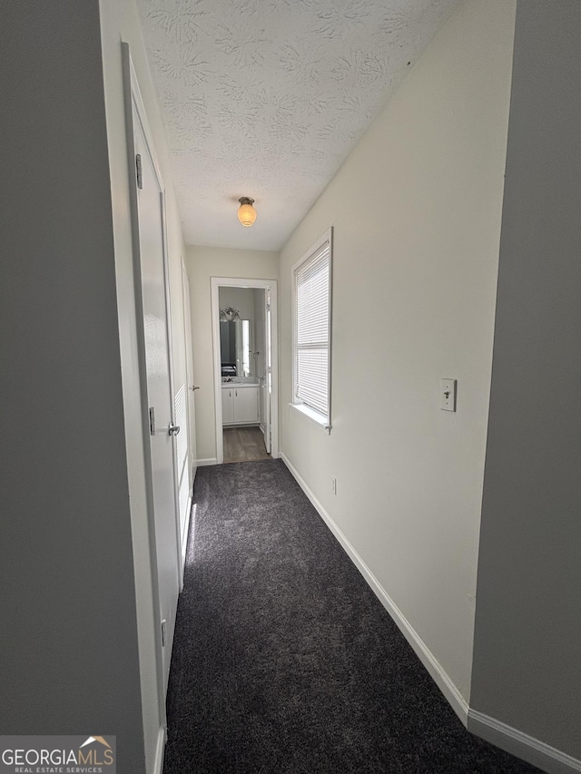 hall featuring dark carpet and a textured ceiling