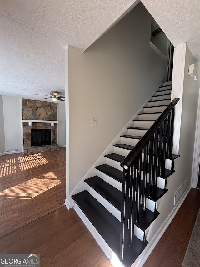 staircase featuring wood-type flooring, ceiling fan, a textured ceiling, and a fireplace