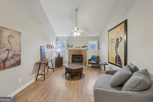 living room featuring ceiling fan, lofted ceiling, light wood-type flooring, and a brick fireplace