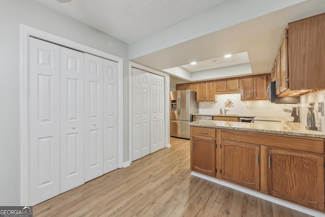 kitchen with stainless steel fridge with ice dispenser, stove, light stone counters, a tray ceiling, and light hardwood / wood-style flooring