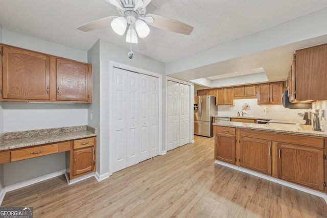 kitchen with built in desk, stainless steel fridge with ice dispenser, light hardwood / wood-style flooring, ceiling fan, and light stone countertops