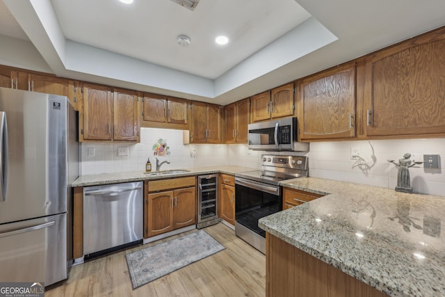 kitchen with wine cooler, sink, light stone counters, light wood-type flooring, and stainless steel appliances