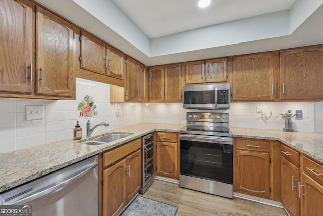 kitchen with sink, light hardwood / wood-style flooring, appliances with stainless steel finishes, light stone counters, and tasteful backsplash