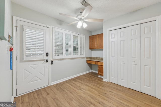 doorway to outside featuring built in desk, a textured ceiling, ceiling fan, and light hardwood / wood-style flooring