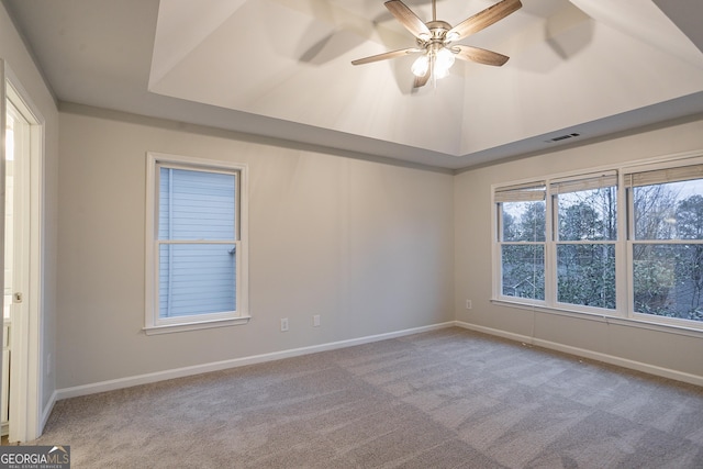 carpeted spare room with ceiling fan, a tray ceiling, and vaulted ceiling