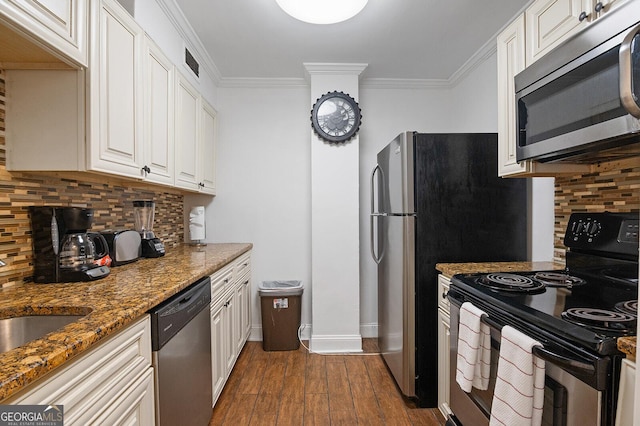 kitchen featuring dark wood-type flooring, appliances with stainless steel finishes, white cabinetry, dark stone countertops, and ornamental molding