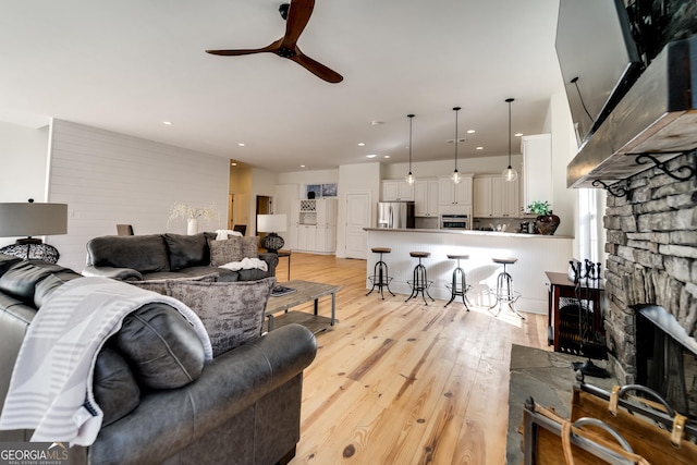 living room featuring a stone fireplace, light hardwood / wood-style flooring, and ceiling fan