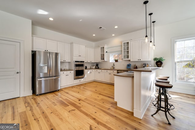 kitchen with appliances with stainless steel finishes, a kitchen breakfast bar, pendant lighting, light hardwood / wood-style floors, and white cabinets