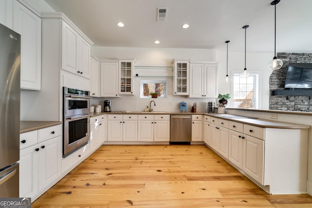 kitchen featuring stainless steel appliances, decorative light fixtures, sink, and white cabinets