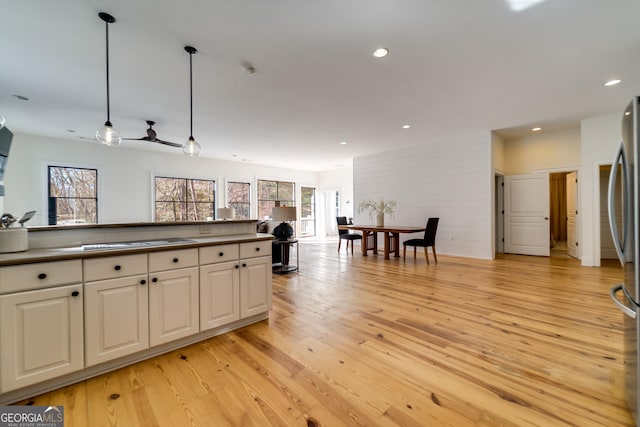 kitchen with cooktop, white cabinetry, hanging light fixtures, stainless steel refrigerator, and light hardwood / wood-style floors