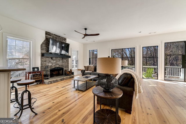 living room featuring ceiling fan, a stone fireplace, and light hardwood / wood-style floors