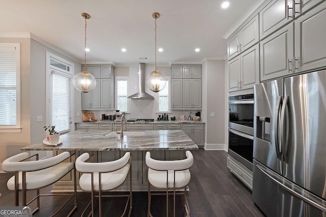 kitchen with appliances with stainless steel finishes, gray cabinetry, light stone counters, and wall chimney exhaust hood