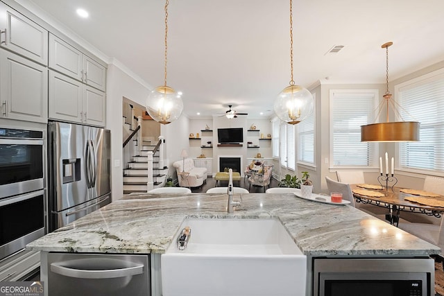 kitchen featuring ornamental molding, appliances with stainless steel finishes, pendant lighting, ceiling fan, and a kitchen island with sink