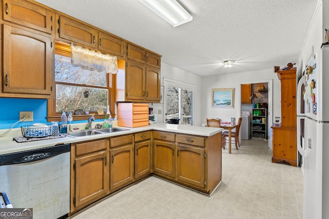 kitchen with sink, white refrigerator, washer / clothes dryer, stainless steel dishwasher, and kitchen peninsula