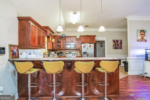 kitchen featuring crown molding, appliances with stainless steel finishes, decorative light fixtures, and a kitchen bar