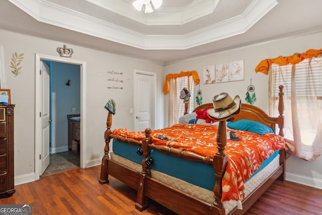 bedroom with ornamental molding, ensuite bath, dark hardwood / wood-style flooring, and a tray ceiling