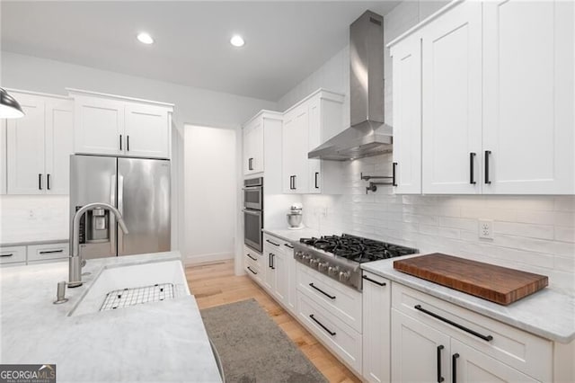 kitchen with light stone counters, white cabinets, wall chimney exhaust hood, and appliances with stainless steel finishes