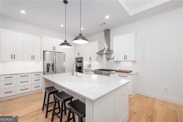 kitchen featuring white cabinetry, stainless steel appliances, a kitchen island with sink, and wall chimney range hood