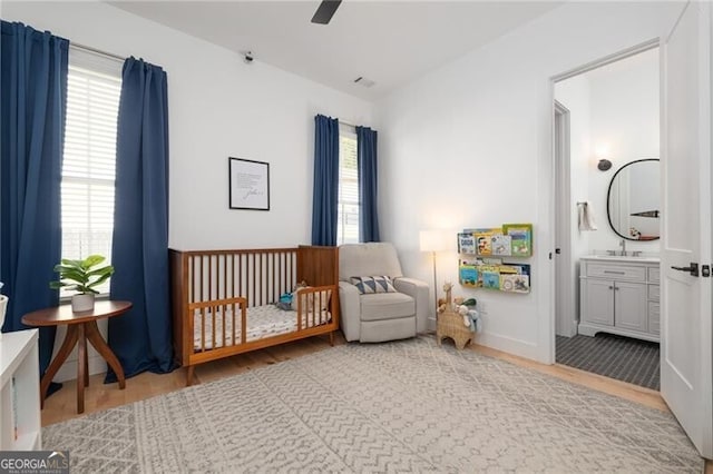 bedroom featuring multiple windows, a crib, wood-type flooring, and ensuite bathroom