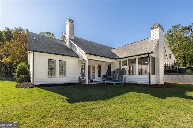 back of house featuring a yard, a sunroom, and a trampoline