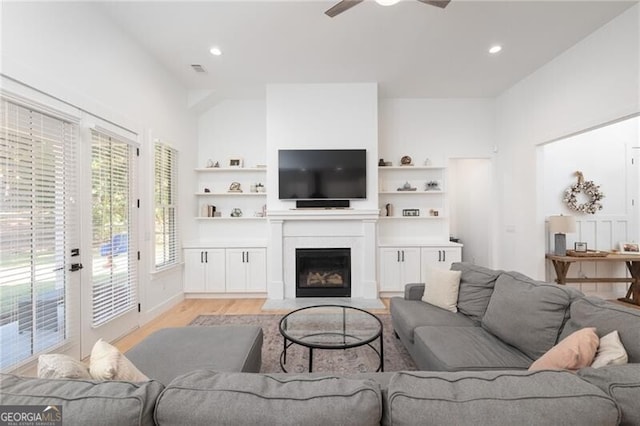 living room with built in features, ceiling fan, and light wood-type flooring