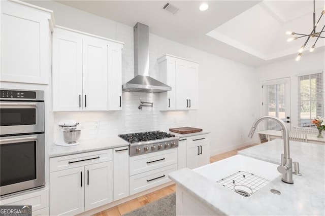 kitchen featuring wall chimney exhaust hood, white cabinetry, light wood-type flooring, stainless steel appliances, and decorative backsplash