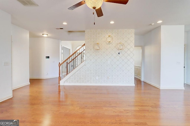 unfurnished living room featuring stairs, visible vents, light wood-style flooring, and an accent wall