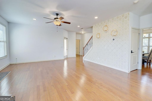 unfurnished living room with an accent wall, stairway, wood finished floors, and wallpapered walls