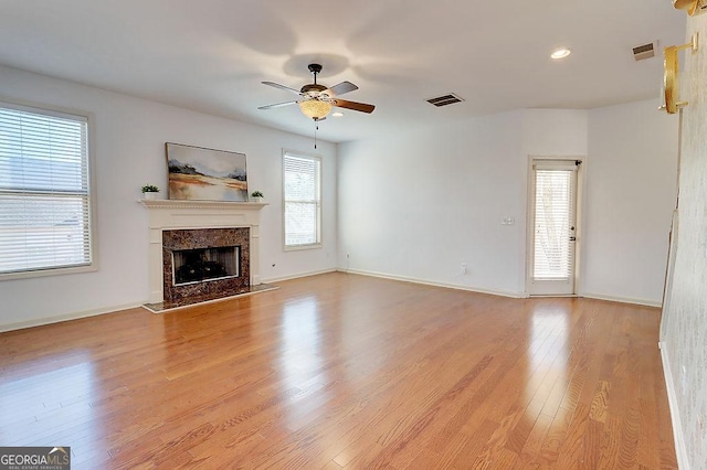 unfurnished living room with ceiling fan, light wood-style floors, visible vents, and a premium fireplace