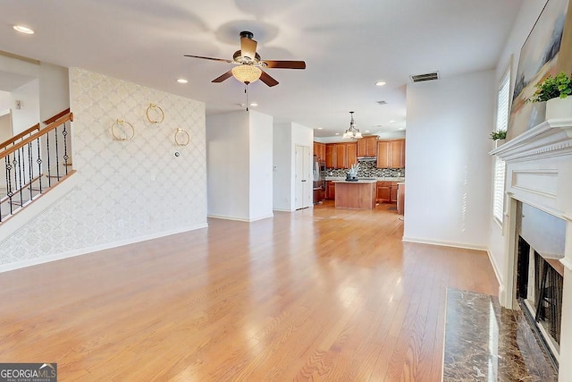 unfurnished living room with visible vents, a fireplace with flush hearth, light wood-style flooring, stairway, and wallpapered walls