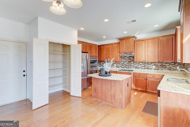 kitchen with visible vents, a sink, under cabinet range hood, light wood-style floors, and appliances with stainless steel finishes