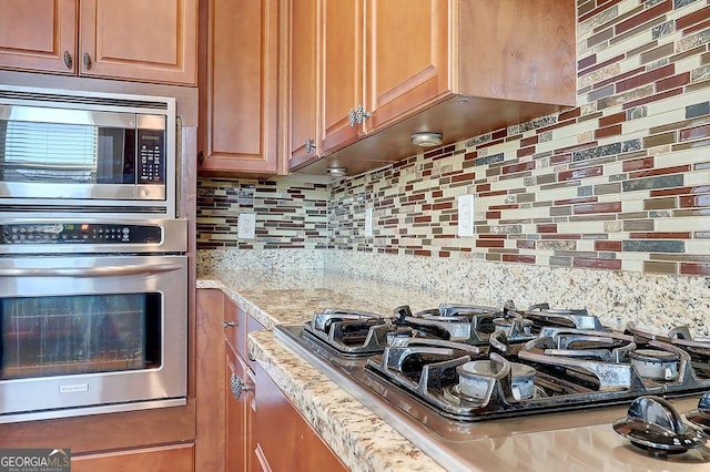 kitchen with tasteful backsplash, brown cabinets, appliances with stainless steel finishes, and light stone counters