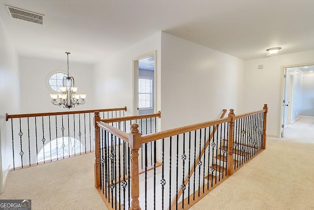 corridor with a notable chandelier, an upstairs landing, visible vents, and carpet floors