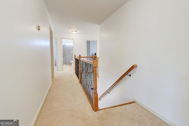 hall featuring an upstairs landing, light carpet, and baseboards