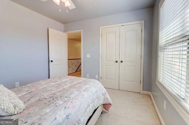 bedroom with a closet, light colored carpet, baseboards, and ceiling fan