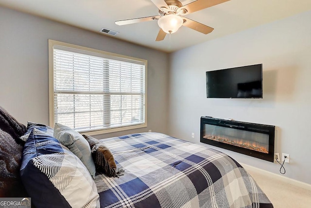 carpeted bedroom featuring a glass covered fireplace, a ceiling fan, and visible vents